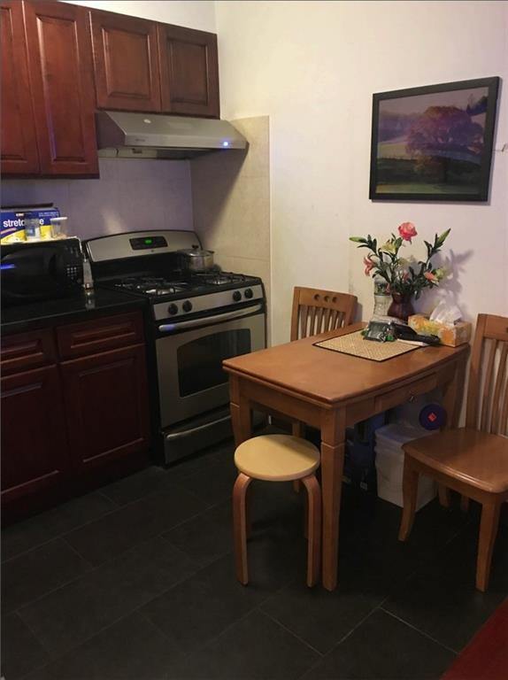 947 55th St Unit 4B, Brooklyn, NY 11219 - kitchen with stainless steel gas stove, under cabinet range hood, dark tile patterned flooring, and dark countertops