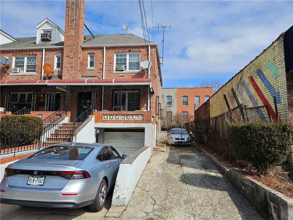 view of property featuring an attached garage, brick siding, fence, driveway, and a chimney