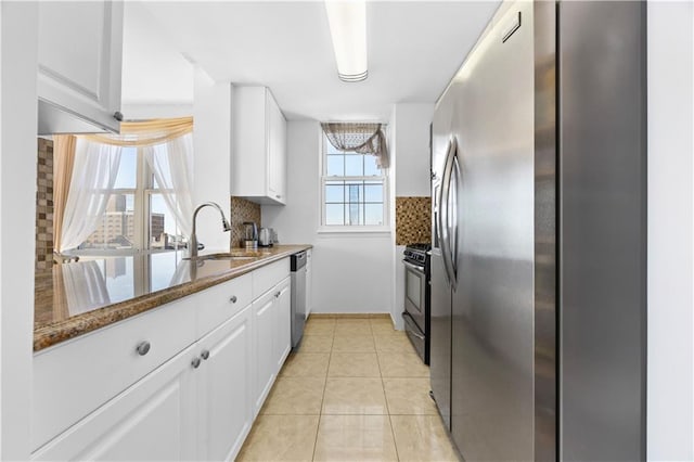 kitchen with light tile patterned flooring, a sink, white cabinets, appliances with stainless steel finishes, and backsplash