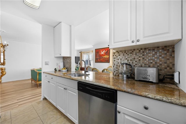 kitchen with decorative backsplash, dark stone countertops, stainless steel dishwasher, white cabinetry, and a sink