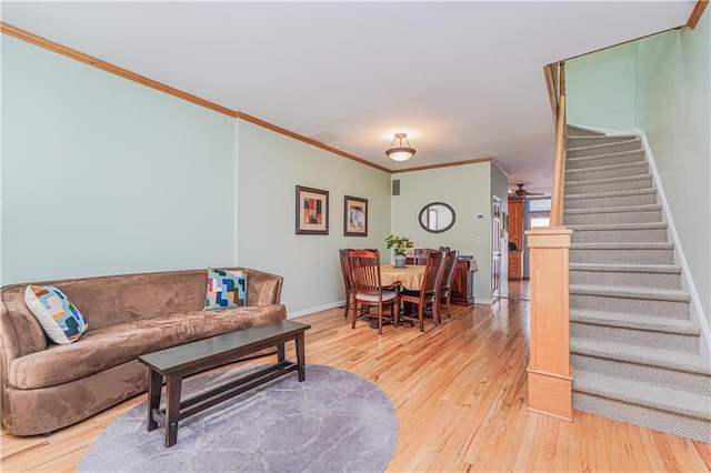 living area with crown molding, stairway, hardwood / wood-style floors, ceiling fan, and baseboards