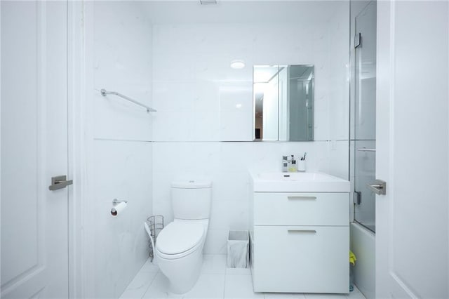 bathroom featuring bath / shower combo with glass door, vanity, toilet, and tile walls