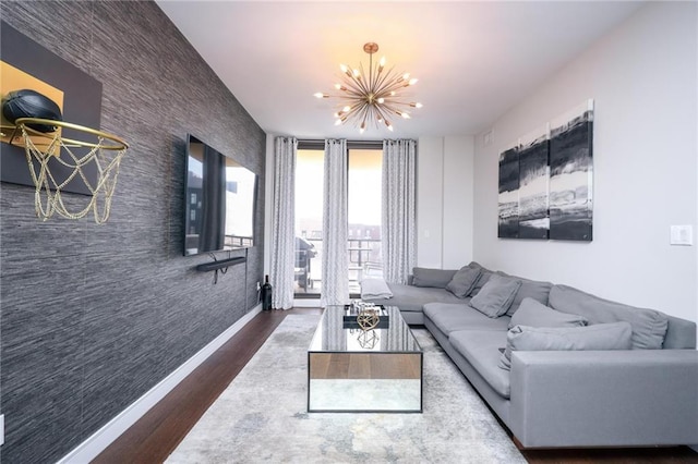 living room featuring an accent wall, a notable chandelier, baseboards, and wood finished floors