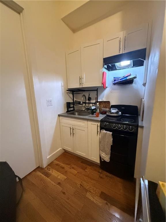 kitchen with dark wood-type flooring, white cabinetry, a sink, black stove, and under cabinet range hood