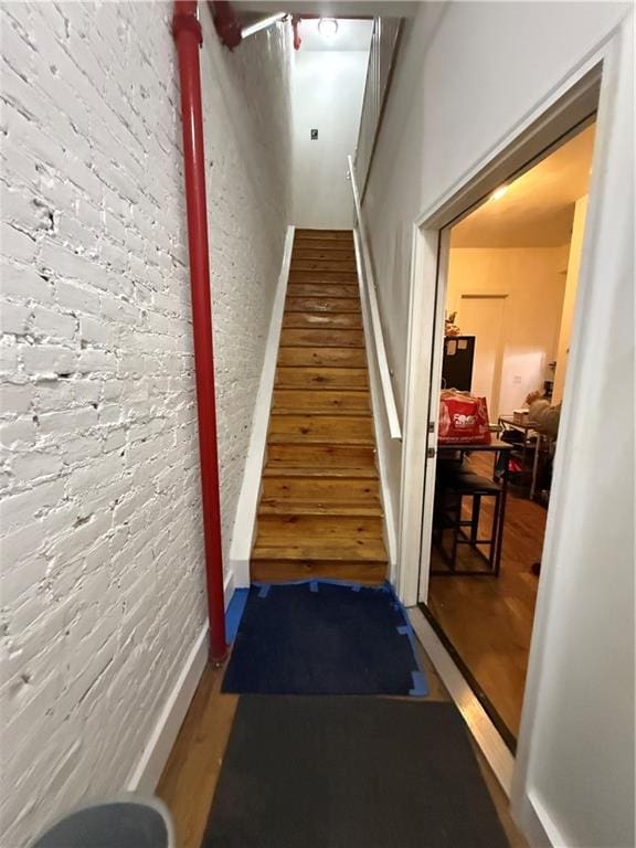 stairs with brick wall and wood finished floors