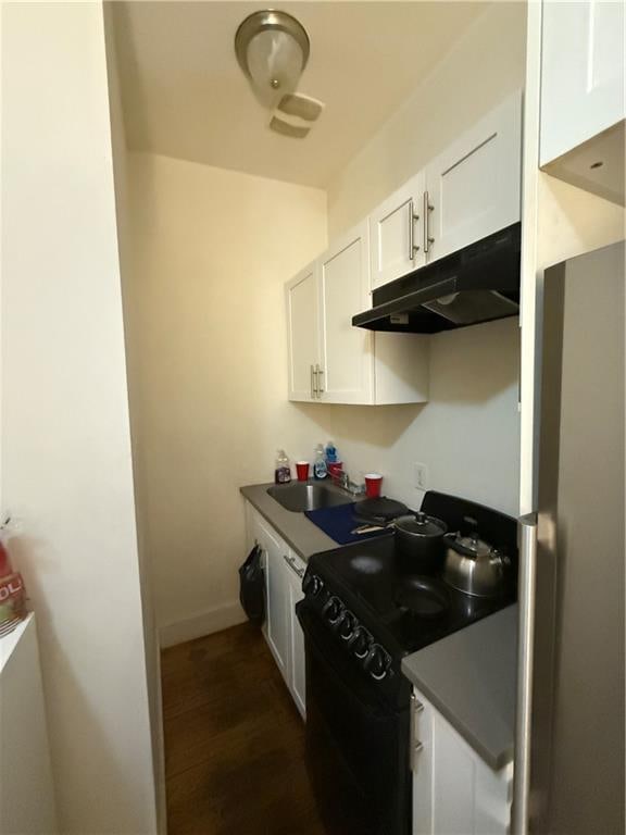 kitchen featuring black gas range, freestanding refrigerator, white cabinetry, a sink, and under cabinet range hood