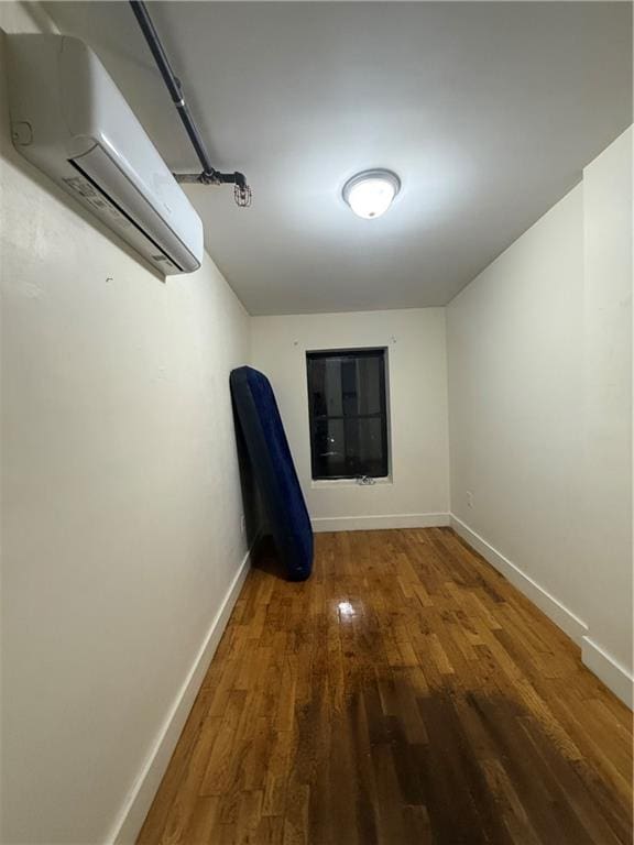 spare room with a wall unit AC, baseboards, and wood finished floors