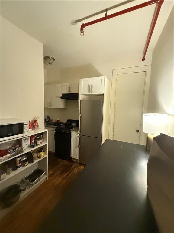 kitchen with black range with gas cooktop, white microwave, refrigerator, under cabinet range hood, and white cabinetry