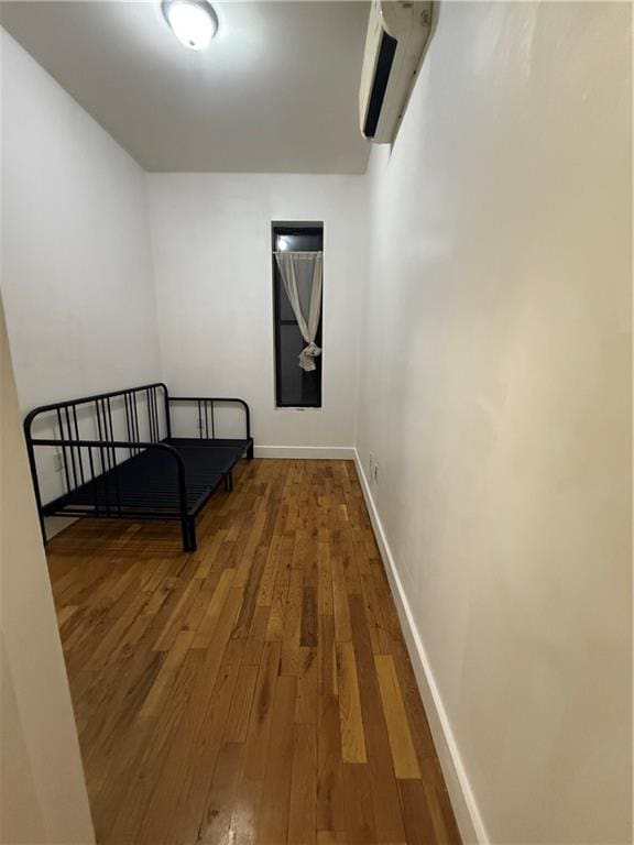 corridor with a wall mounted AC, wood-type flooring, and baseboards