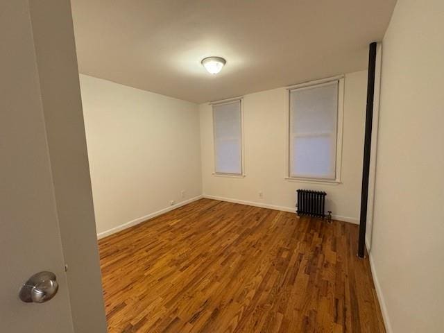 empty room with radiator, baseboards, and wood finished floors