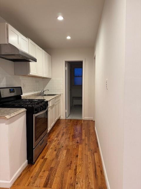 kitchen with stainless steel range with gas cooktop, radiator, light countertops, and white cabinets