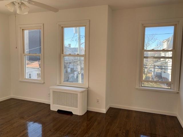 unfurnished room with plenty of natural light, radiator heating unit, and dark wood finished floors