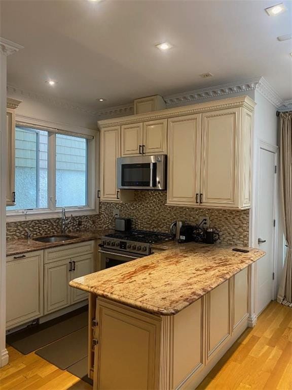 kitchen with backsplash, light wood-type flooring, a peninsula, stainless steel appliances, and a sink