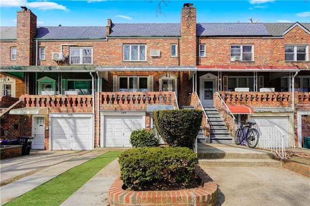 view of property featuring driveway, a chimney, stairway, an attached garage, and brick siding