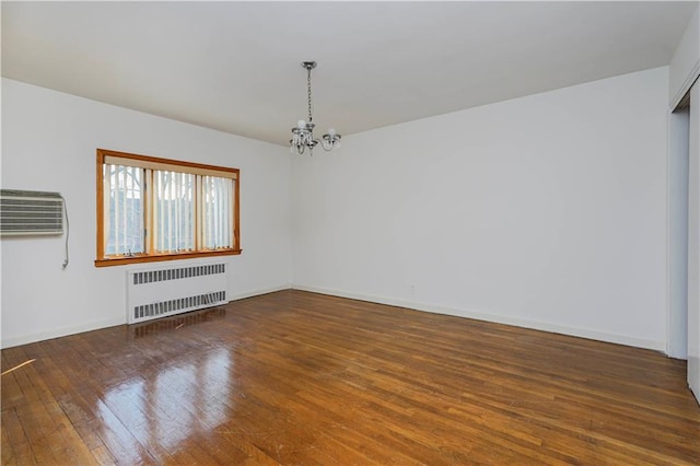 empty room featuring a chandelier, a wall unit AC, hardwood / wood-style flooring, baseboards, and radiator