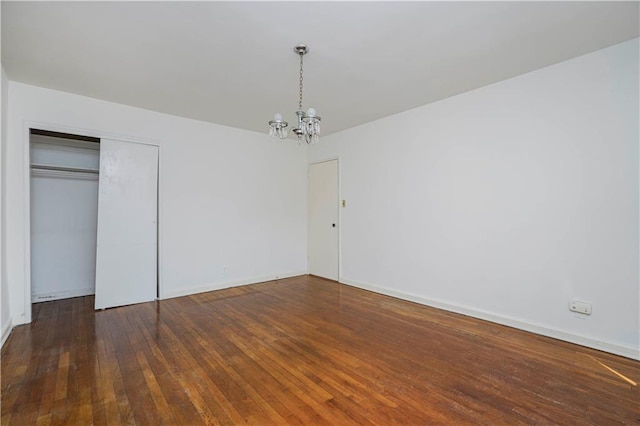 unfurnished bedroom with baseboards, a closet, hardwood / wood-style flooring, and a notable chandelier