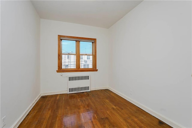 spare room featuring dark wood-style floors, baseboards, and radiator heating unit