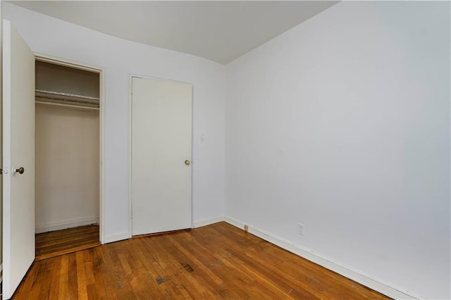 unfurnished bedroom featuring dark wood-style flooring, a closet, and baseboards