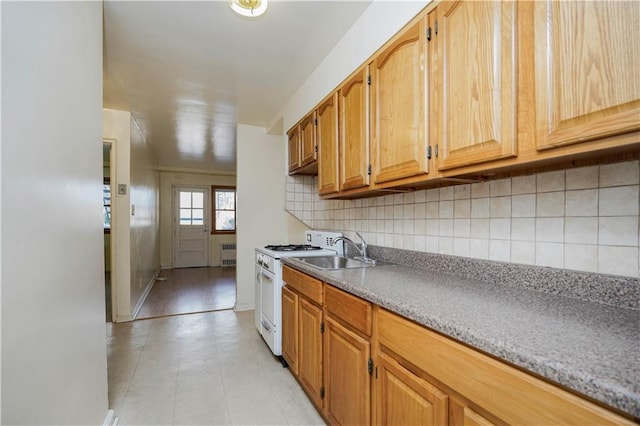 kitchen featuring light countertops, backsplash, radiator heating unit, a sink, and white range with gas stovetop