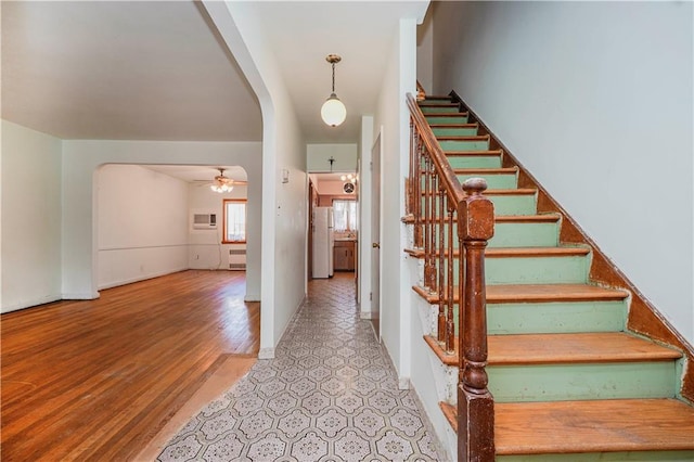 stairs with ceiling fan, arched walkways, radiator heating unit, and wood finished floors