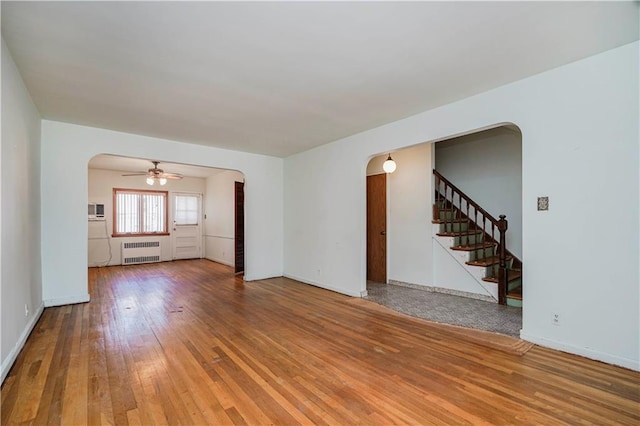 spare room with arched walkways, stairway, radiator heating unit, and hardwood / wood-style flooring