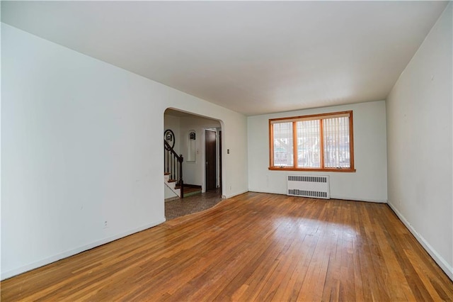 empty room featuring arched walkways, baseboards, stairs, radiator, and hardwood / wood-style floors