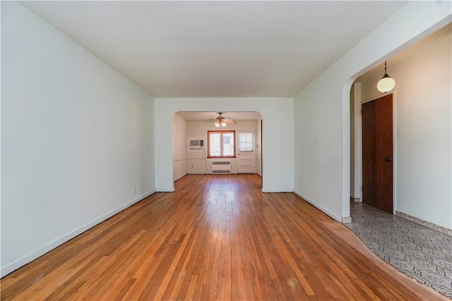 unfurnished room featuring arched walkways, baseboards, light wood-style floors, radiator, and a wall mounted air conditioner