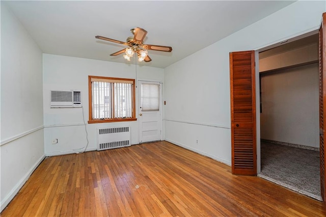 interior space with baseboards, ceiling fan, radiator heating unit, wood-type flooring, and a wall mounted AC