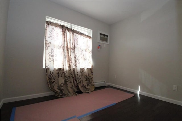 empty room with a baseboard radiator, baseboards, wood finished floors, and an AC wall unit