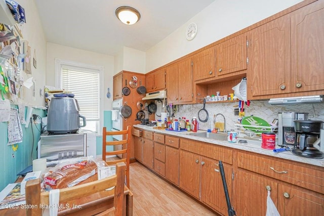 kitchen featuring brown cabinets, light wood finished floors, light countertops, decorative backsplash, and a sink