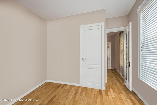 unfurnished room with light wood-style floors, a wealth of natural light, and baseboards