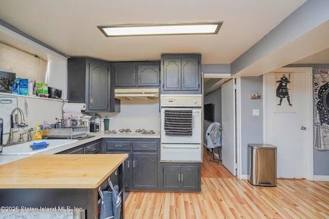 kitchen featuring white appliances, light wood-style floors, under cabinet range hood, a sink, and a warming drawer