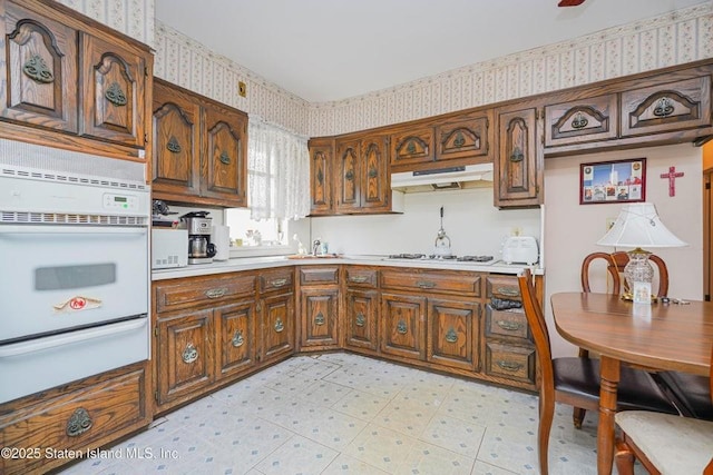 kitchen with a warming drawer, light floors, white appliances, under cabinet range hood, and wallpapered walls