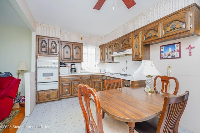 kitchen featuring white appliances, wallpapered walls, light floors, under cabinet range hood, and a warming drawer