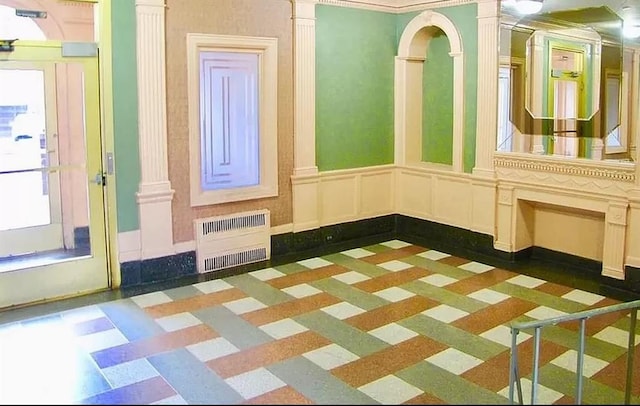 interior space with a wainscoted wall, radiator heating unit, a decorative wall, and ornate columns