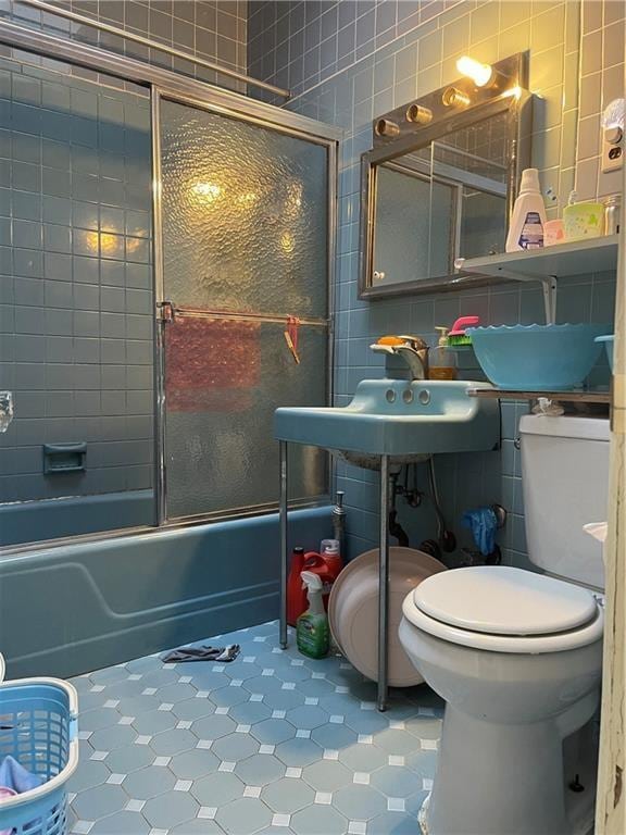 full bathroom featuring shower / bath combination with glass door, tile walls, toilet, a sink, and tile patterned floors