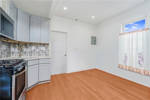 kitchen featuring light wood-type flooring, appliances with stainless steel finishes, light countertops, decorative backsplash, and baseboards