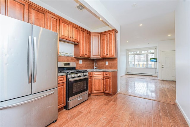 kitchen with tasteful backsplash, light wood-type flooring, appliances with stainless steel finishes, brown cabinetry, and a sink