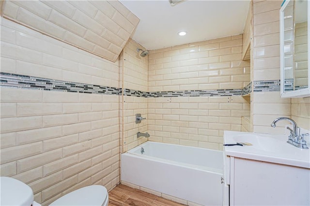 bathroom featuring washtub / shower combination, toilet, vanity, wood finished floors, and tile walls