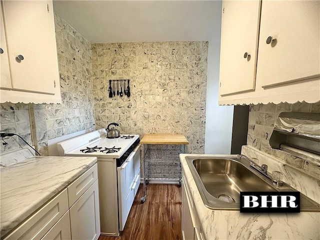 kitchen featuring dark wood-type flooring, light countertops, white gas stove, white cabinetry, and a sink