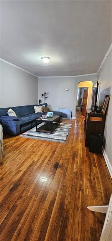 living area with arched walkways, baseboards, crown molding, and hardwood / wood-style floors