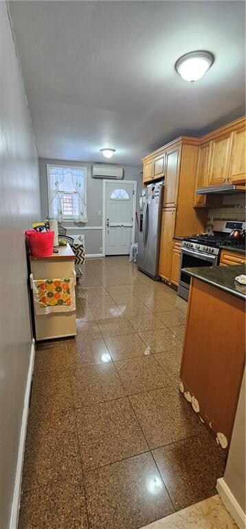 kitchen featuring appliances with stainless steel finishes, an AC wall unit, under cabinet range hood, and baseboards