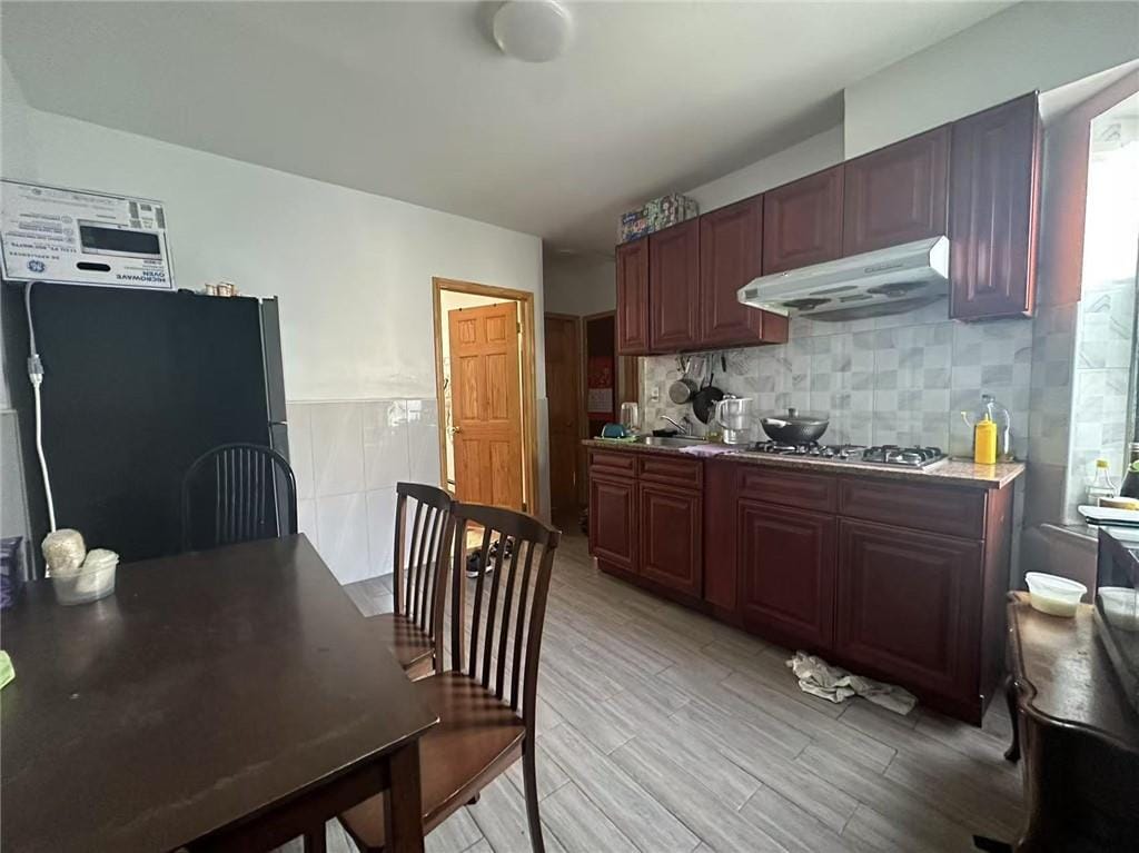 kitchen with tasteful backsplash, freestanding refrigerator, light wood-type flooring, under cabinet range hood, and stainless steel gas stovetop