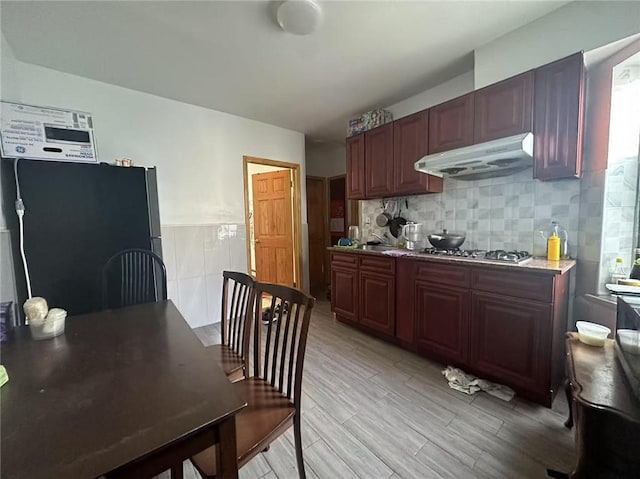 kitchen with under cabinet range hood, backsplash, stainless steel gas stovetop, light wood finished floors, and freestanding refrigerator