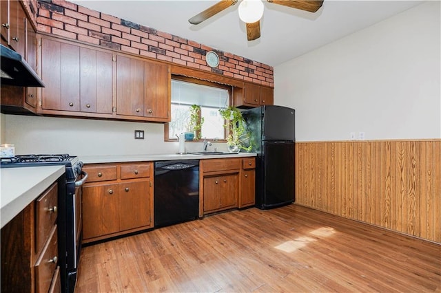 kitchen with light wood-style flooring, under cabinet range hood, a wainscoted wall, light countertops, and black appliances