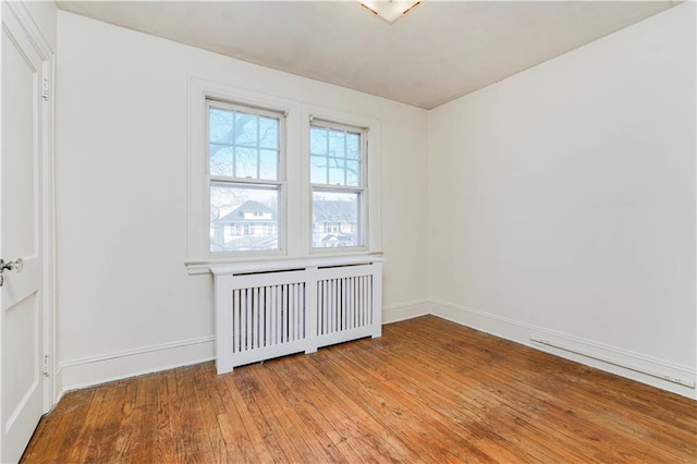 spare room featuring light wood-type flooring, baseboards, and radiator heating unit