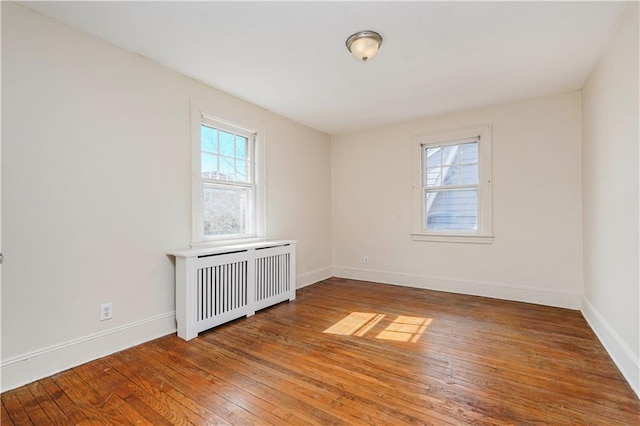 unfurnished room with baseboards, radiator heating unit, and hardwood / wood-style flooring