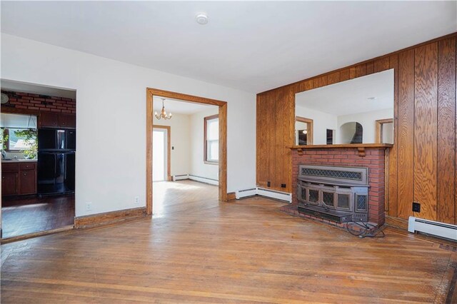 unfurnished living room featuring wooden walls, baseboard heating, and wood finished floors