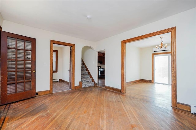 empty room with hardwood / wood-style flooring, a baseboard radiator, stairway, and baseboards