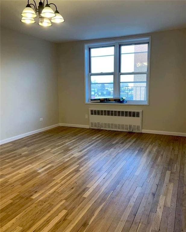 unfurnished room featuring baseboards, a notable chandelier, radiator heating unit, and hardwood / wood-style flooring